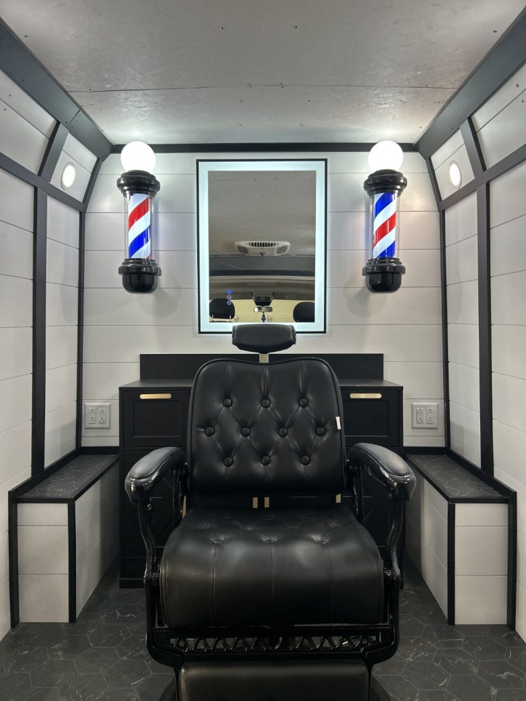 Black tufted leather barber chair inside the Barber Mobile with illuminated barber poles, backlit mirror, and shiplap walls built by Alexander's RV