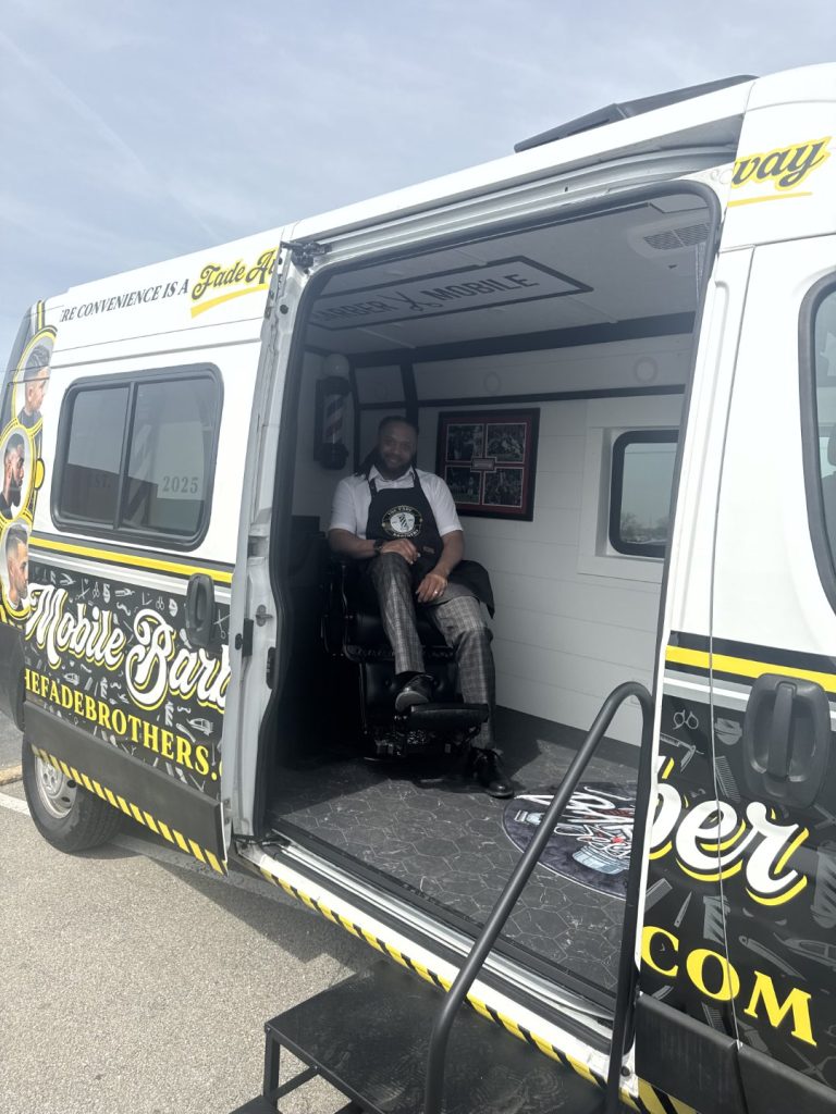 The Fade Brothers Barber Mobile van with doors open showing the finished barbershop interior and full custom vehicle wrap with gold and black branding, built by Alexander's RV