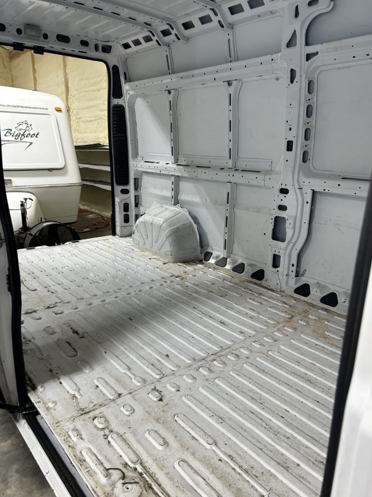 Empty white cargo van interior with bare metal floor and exposed wall panels before mobile barbershop conversion by Alexander's RV